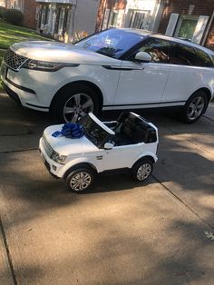 a white range rover parked in front of a house next to a car with a blue bow on it