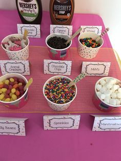 a table topped with ice cream and desserts on top of a pink table cloth