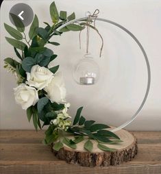 white flowers and greenery are arranged in front of a circular light fixture on a wooden table