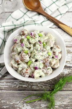 a white bowl filled with potato salad next to a wooden spoon