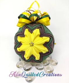 an ornament with yellow flowers and green ribbon on it's top is surrounded by crystal stones