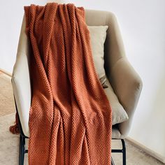 an orange blanket sitting on top of a chair next to a white wall with the words rust winter throw