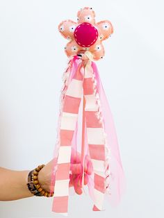 a hand holding a pink and white striped ribbon with an object in the middle that looks like a flower