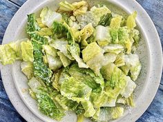 a white bowl filled with lettuce on top of a blue wooden tablecloth