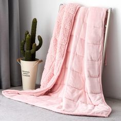 a pink blanket sitting on top of a chair next to a cactus