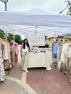 a woman standing next to a table with clothes on it under a white tent outside