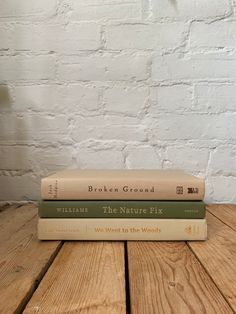 three books stacked on top of each other in front of a white brick wall and wooden floor