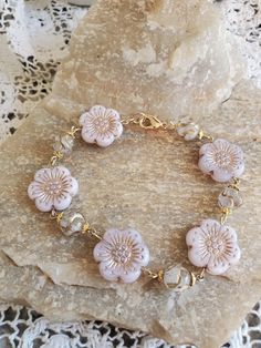 a bracelet with flowers on it sitting on top of a piece of lace next to a rock