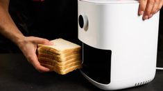 a person holding a piece of bread in front of a toaster