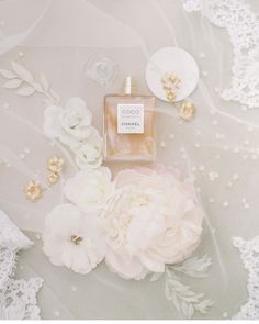 a bottle of perfume sitting on top of a table next to white and gold flowers