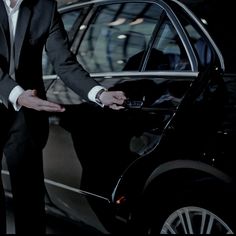 a man in a tuxedo standing next to a car with his hands out