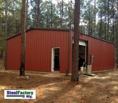 a red building in the middle of a forest with trees around it and a man standing outside