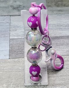 a purple and white beaded keychain with pink hearts on it sitting in a clear box