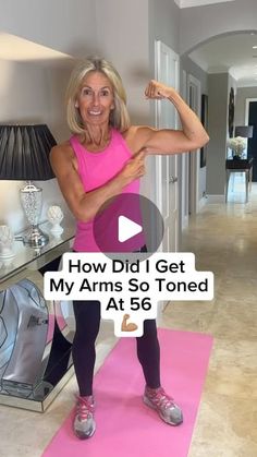 a woman standing on top of a pink mat in front of a mirror and holding her arm up