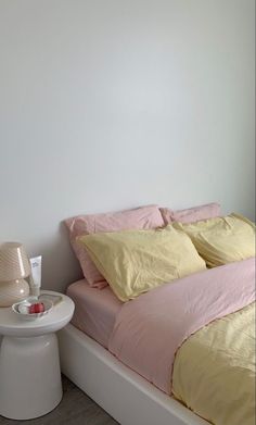 a bed with pink and yellow sheets in a bedroom next to a night stand on the floor