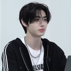 a young man sitting in front of a laptop computer wearing a black jacket and white t - shirt