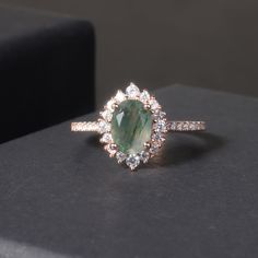 Experience true vintage charm with our Oval Shaped Vintage Moss Agate Halo Engagement Ring. Featuring a unique oval-shaped moss agate stone surrounded by a halo of sparkling diamonds, this ring is the perfect blend of old-world elegance and modern glamour. Romance and sophistication meet in this stunning piece. Main Stone: Moss Agate, 6x8mm  Side Stones: Colourless Zircon Accents VS to VVS clarity Band: 1.0-1.2mm bandwidth. Band Material: 14k Gold, 18k Gold, Platinum Conflict-Free ** This item i Custom Gemstone Rings, Agate Wedding Ring, Vintage Jewellery Rings, Agate Ring, Halo Engagement Ring, Halo Engagement, Everyday Jewelry, Moss Agate, Sparkle Diamonds