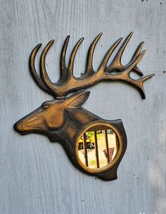 a metal deer head mounted to the side of a wooden wall with a mirror in it's mouth