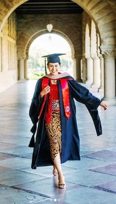 a woman in graduation gown and cap is walking through an archway with her arms outstretched