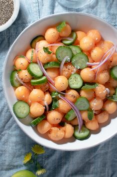 a white bowl filled with cucumbers, onions and carrots on top of a blue table cloth