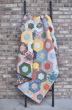 a multicolored patchwork quilt hanging up against a brick wall