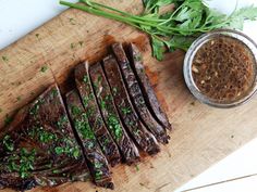 steak sliced up on a cutting board with parsley and seasoning next to it