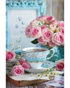 a tea cup and saucer on a table with pink roses in front of it