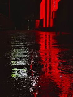 a red light reflecting off the water in front of a tall building at night time