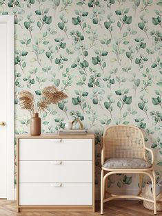 a white dresser sitting next to a wall with green leaves on it and a chair in front of it