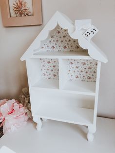 a white doll house sitting on top of a table next to a pink flower arrangement