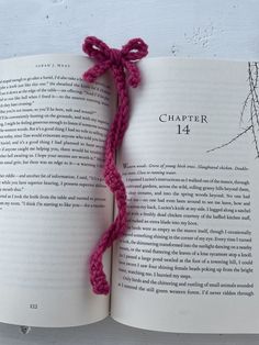 an open book with a pink crochet tie on it