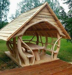 a wooden structure made out of logs with benches under it on a deck in the middle of a grassy area