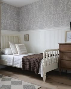 a white bed sitting next to a wooden dresser in a bedroom on top of a hard wood floor