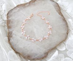 a rose gold bracelet with crystal stones on top of a white lace covered rock,