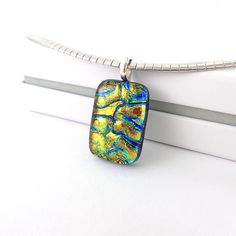 This unique petite dichroic glass pendant has immense depth of colours finished with a clear glass and hand polished to smooth.  Featuring yellow golden glass with veins of cobalt blue, and lime green it is a real stunner that slightly changes colour depending on the angle of light. This pendant is approximately 1 inch long, mounted on a silver plated bail. It will arrive wrapped in tissue paper inside a small gift ouch.  A lovely one of a kind gift for someone special. **This is a pendant only, chain is not included. More original dichroic glass pieces: https://www.etsy.com/uk/shop/LeanneStreet?ref=seller-platform-mcnav Modern Rectangular Glass Jewelry, Iridescent Glass Jewelry As Gift, Iridescent Glass Jewelry Gift, Iridescent Glass Jewelry For Gifts, Modern Murano Glass Jewelry Gift, Modern Murano Glass Jewelry As Gift, Handmade Pendant Necklace, Dichroic Glass Pendant, Fused Glass Jewelry