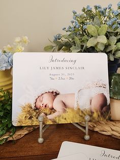 a baby announcement card sitting on top of a wooden table next to flowers and potted plants