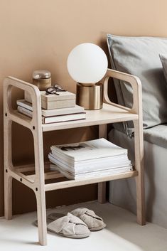 a small wooden shelf with books on it next to a lamp and slippers in front of a bed