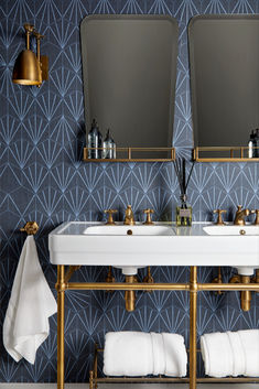 two sinks and mirrors in a bathroom with blue wallpaper, gold fixtures and white towels