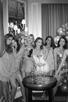 a group of women standing next to each other in front of a cake and balloons