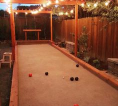 an outdoor bowling alley with lights strung over the top and balls on the ground in front