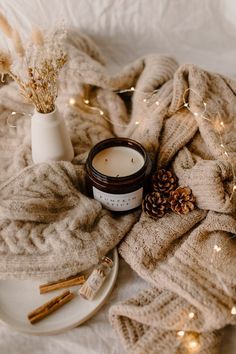 a white plate topped with a candle next to a blanket and some candles on top of it