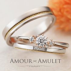 two wedding rings with one diamond on top and the other in gold, sitting next to an orange flower