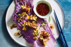 a white plate topped with purple cabbage covered in sauce and some chopsticks next to it