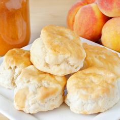 four biscuits on a plate next to some peaches and a jar of honey in the background