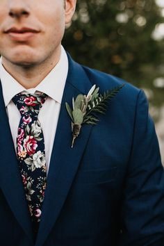 a man wearing a blue suit and flower boutonniere is looking at the camera