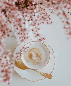 there is a cup and saucer on the table with pink flowers in the background