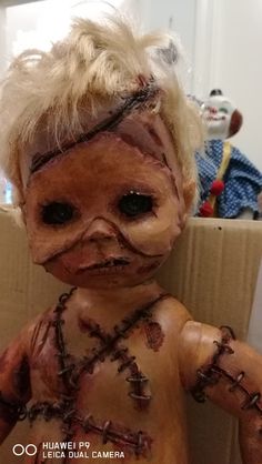 a creepy looking doll with chains on it's face and hands, sitting in front of a cardboard box