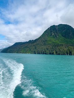 the wake of a boat traveling on blue water with mountains in the backgroud