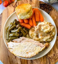 a white plate topped with meat, potatoes and green beans next to some carrots