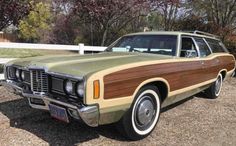 an old station wagon with wood trim parked in front of a white fence and trees